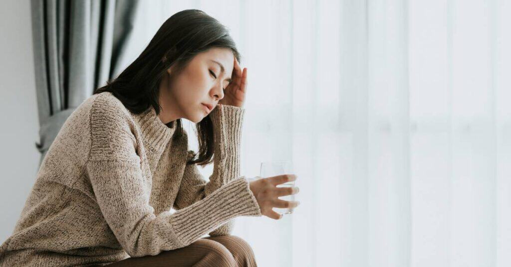 detoks od wiadomości z mediów społecznościowych pochylona kobieta z bólem głowy i szklanką wody